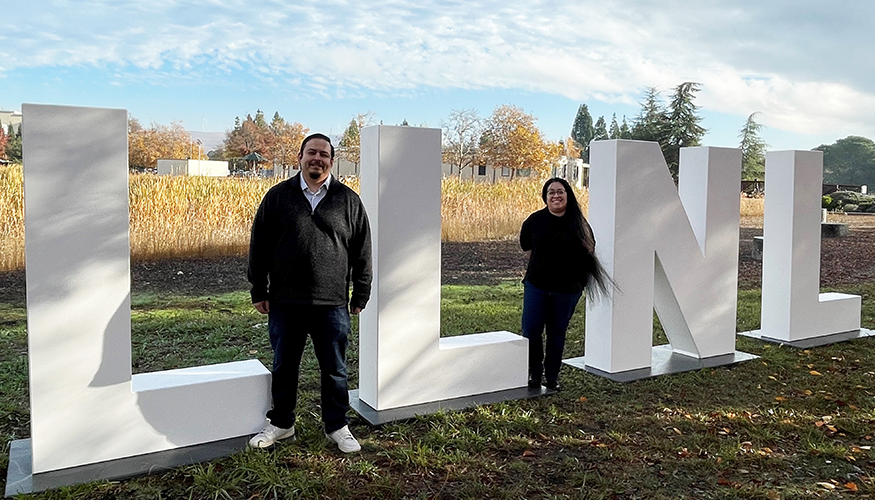 Omar and Mary stand outside by large LLNL letters